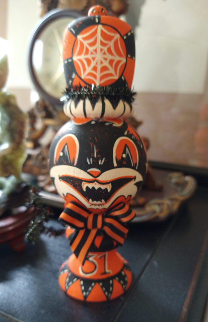 Wooden peg doll with a cat face, painted in vintage Halloween style in orange, black, and white.