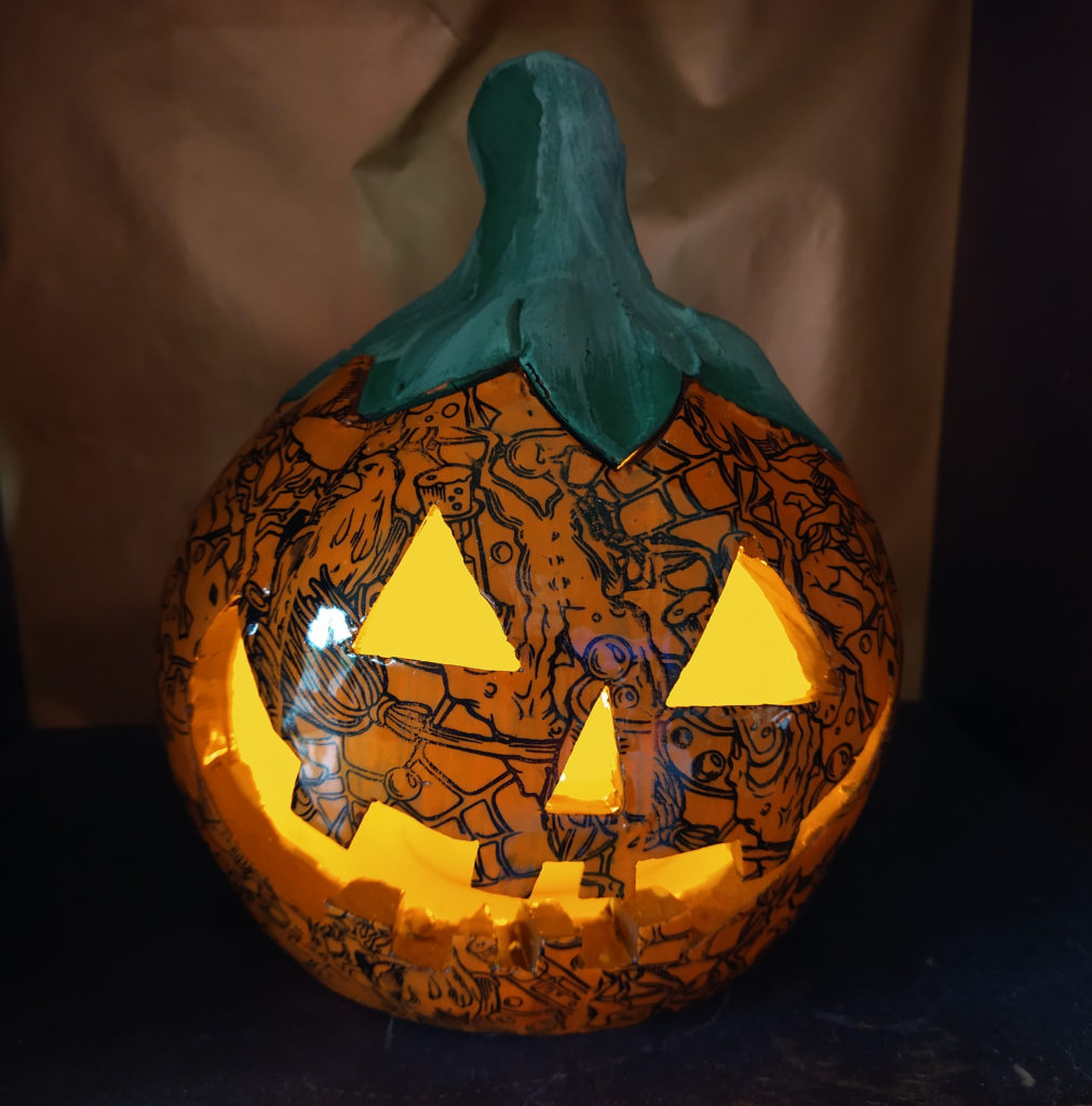 Lit ceramic jackolantern covered with Halloween transfers.