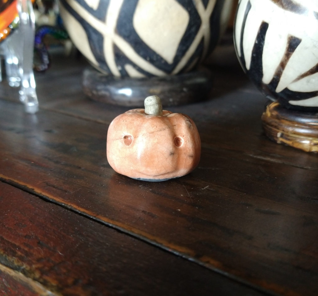 Tiny ceramic pumpkin with serene expression.
