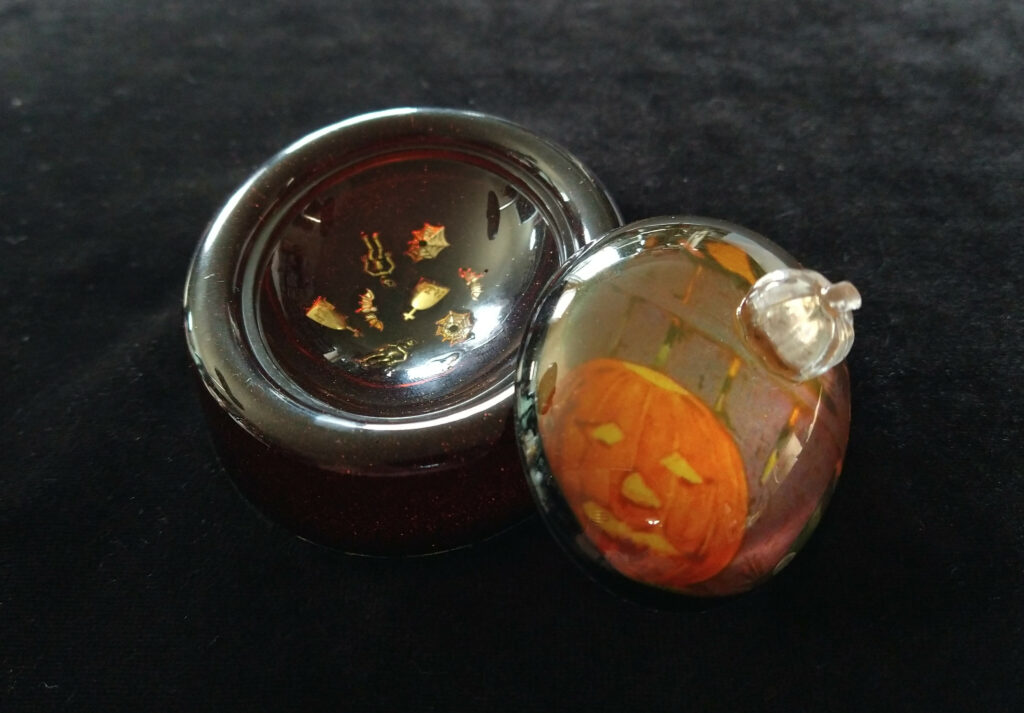 Dark orange resin box with Halloween trinkets embedded in the bottom, with a vintage Halloween lid.