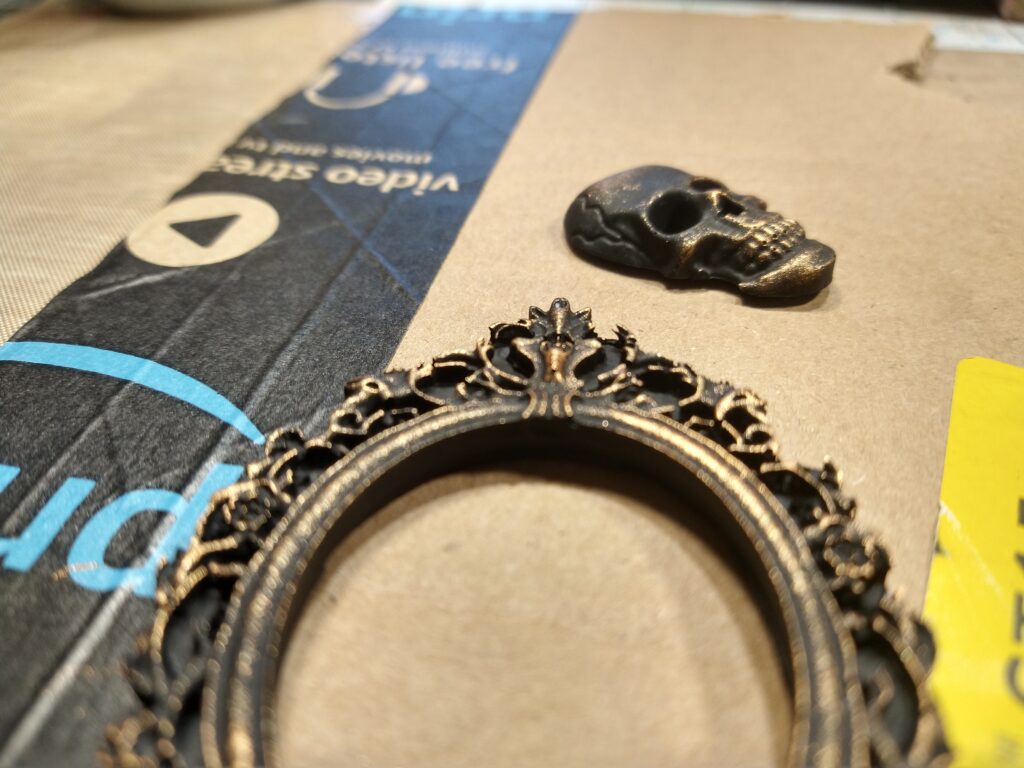 Black and gold frame and skull, sitting on a piece of cardboard to dry.